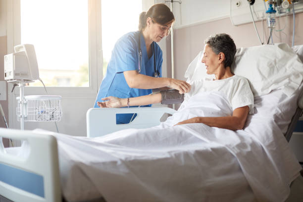Female nurse adjusting the blood pressure monitor on female hospital patient Photo with copy space of female nurse leaning over bedside while attaching the blood pressure armband to a female patient's right arm. hospital patient bed nurse stock pictures, royalty-free photos & images