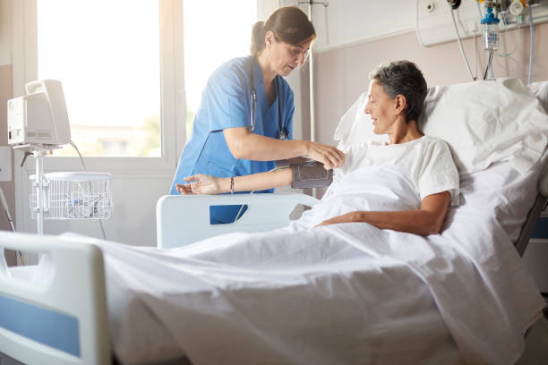 Female nurse adjusting the blood pressure monitor on female hospital patient Photo with copy space of female nurse leaning over bedside while attaching the blood pressure armband to a female patient's right arm. beds stock pictures, royalty-free photos & images