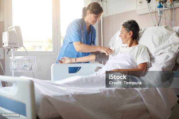 Female Nurse Adjusting The Blood Pressure Monitor On Female Hospital Patient Stock Photo - Download Image Now