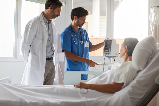 A male doctor and nurse are standing at the bedside of a female hospital patient and all three are carefully looking at the numbers registered on the blood pressure monitor. Copy space available