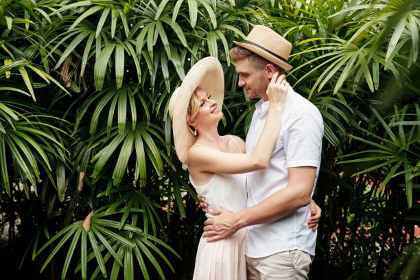 Young lovely couple embracing each other while standing against the tropical green plants