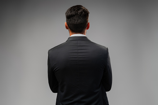 Young businessman from the back standing on gray background in studio