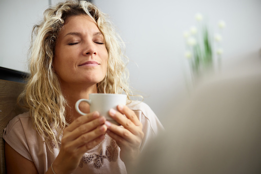 Young woman enjoying in the smell of fresh coffee with her eyes closed at home.