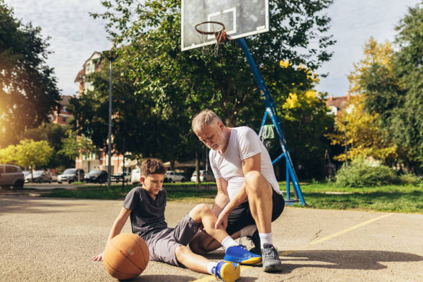 padre che aiuta il ragazzo con un trauma alle gambe dopo aver giocato a basket. infortunio sportivo. - athlete coach basketball male foto e immagini stock