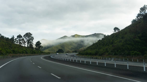Cars travelling on motorway with fog drifting among the hills. Hamilton, New Zealand. Cars travelling on motorway with fog drifting among the hills. Hamilton, New Zealand. waikato region stock pictures, royalty-free photos & images