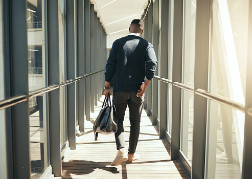 Businessman at airport walking for work travel and male african morning commute to city. Transport service from airplane terminal to hotel, rear view of modern worker carrying hand luggage bag trip.