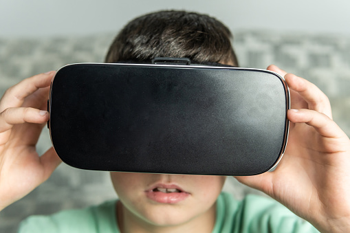 Front view of a dark-haired boy holding and putting on his virtual reality goggles.