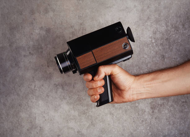 un cineasta irreconocible sosteniendo una antigua cámara de película de película analógica super8, 8mm frente a una pared de hormigón. apuntando a la cámara como un arma - 8mm camera fotografías e imágenes de stock