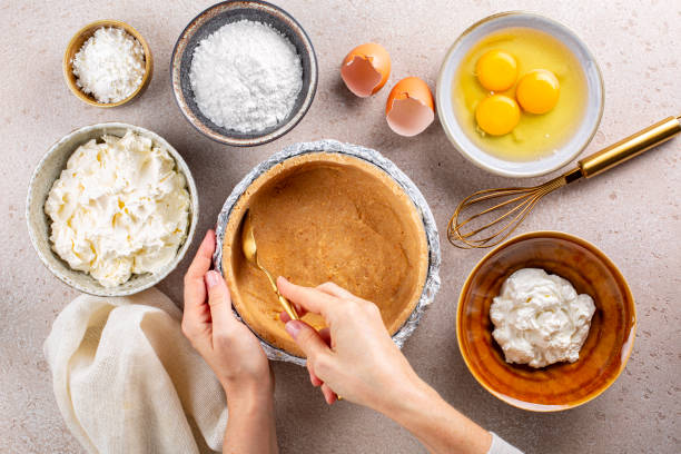 Cooking cheesecake, woman hands making a cake crust from crushed cookies and butter. Main ingredients: soft, fresh cream cheese, eggs, sugar powder, sour cream, corn starch. Top view. stock photo
