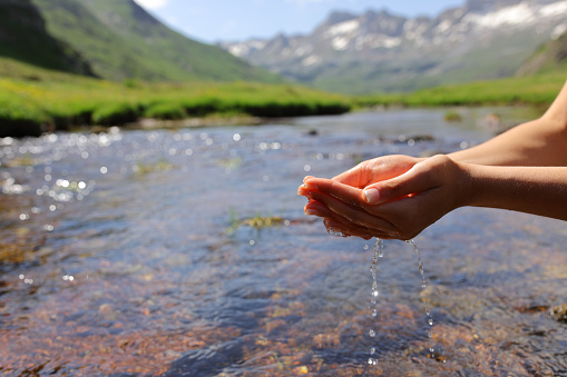 Woman hands catching water from river in the mountain