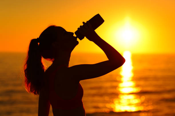 Sportswoman drinking water from bottle at sunset stock photo