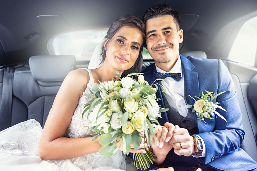 Millennial future bride sitting backseat in small normal car to go for her wedding. Part of a series. She has short hair and is wearing eyeglasses and is looking at the camera with a nervous smile. Horizontal waist up indoors shot with copy space.