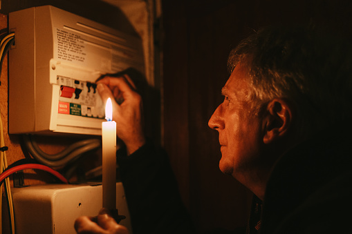 Senior man checking home fuse box by candlelight during power outage
