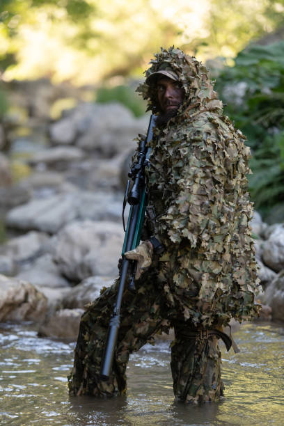 迷彩服を着た軍人またはエアガン奏者が川をこっそりと歩き回り、スナイパーライフルから横または標的を狙う。 - wet spy men suit ストックフォトと画像