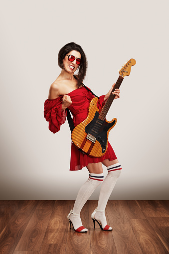 Trendy female rock musician enjoys the music with electric guitar against white background