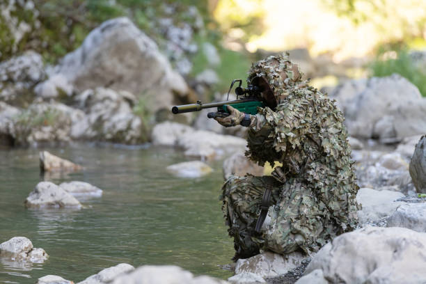 迷彩服を着た軍人またはエアガン奏者が川をこっそりと歩き回り、スナイパーライフルから横または標的を狙う。 - wet spy men suit ストックフォトと画像