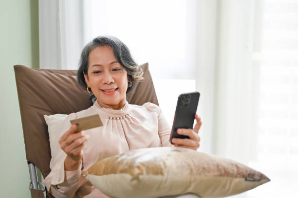 istock Senior Asian female using mobile banking application while relaxing in her living room. 1432152951