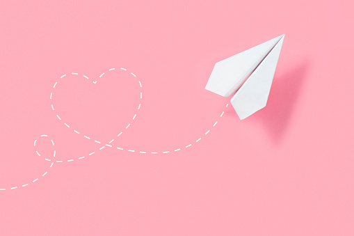 Paper airplane on pink background with heart shaped flight path