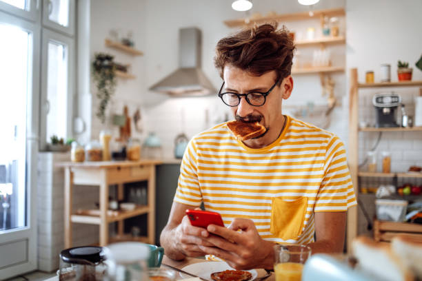 Shot of a mature man using a cellphone while having a breakfast at home stock photo