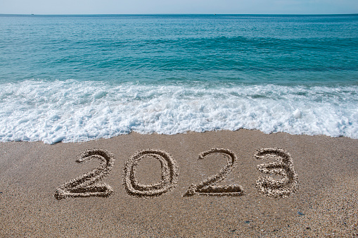 New year 2023 written on sandy beach with waves