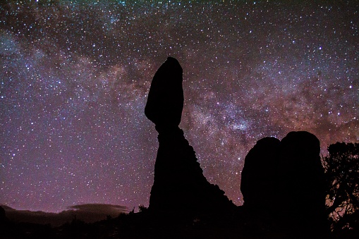 The silhouettes of rock formations under stunning purple galaxy milky way sky in Arches National Park