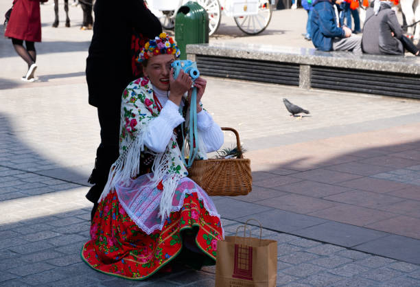Krakow, Lesser Poland, Poland - March 24, 2019: A woman in Polish national costume takes a picture with a Fujifilm instant camera. Main Square of the Old Town of Krakow