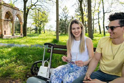 Caucasian couple sitting on the park bench, and resting after traveling, after they arrived in the city
