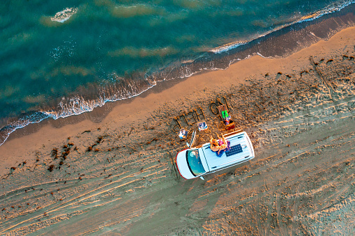Directly above shot of couple relaxing on roof of campervan while enjoying at beach during summer vacation