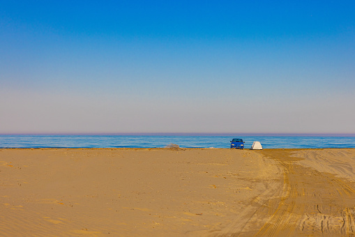 Car parked on sea shore at sandy beach against clear blue sky during sunny day