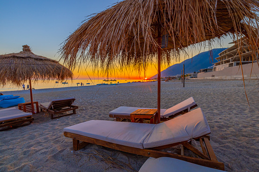 Empty lounge chairs and straw umbrellas at beach against sky during sunset