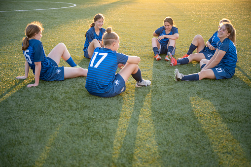 Female football teammates relaxing on field after game during sunset.