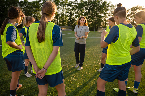 Coach instructing to female football players on soccer field.