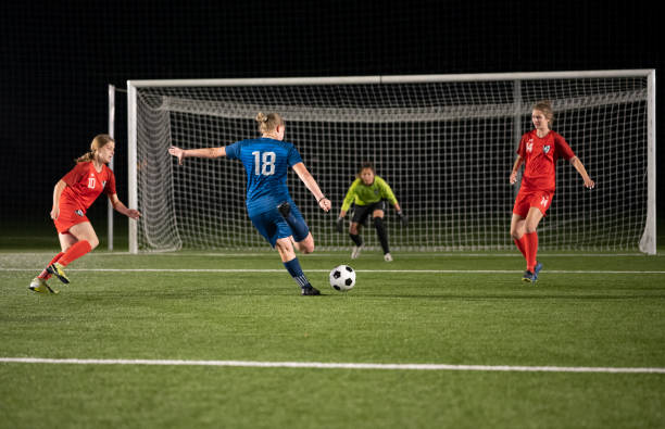 Female football player attempting to kick goal during match at night.