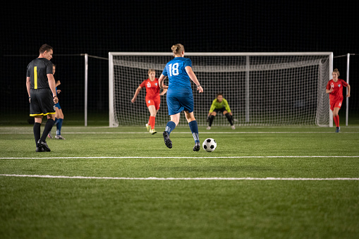 Female football player running to kick goal during match at night.