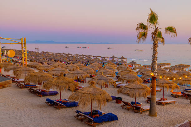 View of lounge chairs and straw umbrellas arranged at beach against sky during sunset