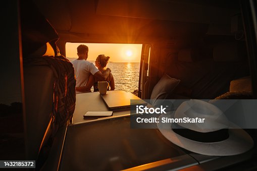 istock Couple enjoying sunset over sea while standing together outside camper trailer 1432185372
