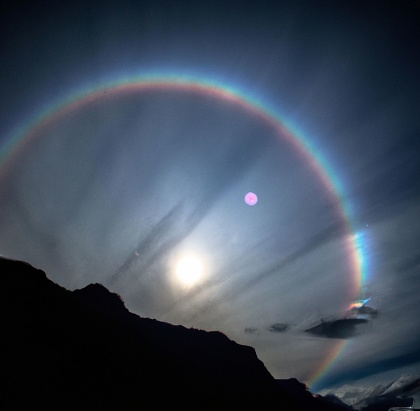 A Moonbow and a shining full moon  in a clear gray sky
