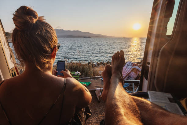 istock Woman using smart phone while relaxing with man in motor home against sea 1432185803
