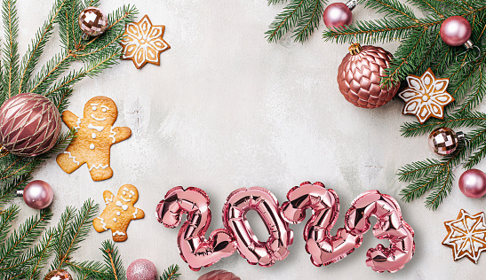 Pink 2023 balloons on wooden background with Christmas shiny balls, decorations, fir tree branches and gifts, flat lay. New Years celebration concept backdrop