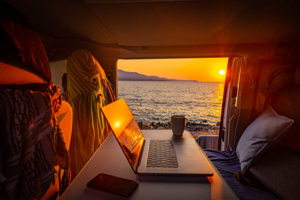 laptop und smartphone durch kaffeetasse im wohnmobil gegen meer während des sonnenuntergangs - campingplatz stock-fotos und bilder