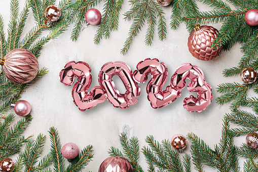 Pink 2023 balloons on wooden background with Christmas shiny balls, decorations, fir tree branches and gifts, flat lay. New Years celebration concept backdrop