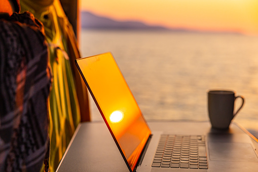 Close-up of orange sunset reflecting on laptop by coffee cup in campervan against sea