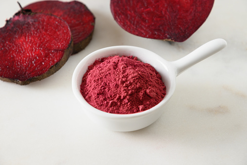 Beetroot powder for cooking healthy beverage in bowl and beetroot vegetable on white marble background. Close up.