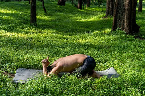 The view of a Hispanic man doing the ardha kurmasans yoga pose on the grass of a park