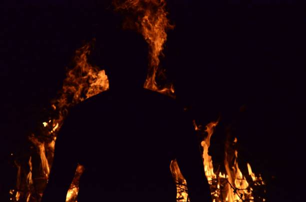 A silhouette of a man seen from behind looking at burning flames