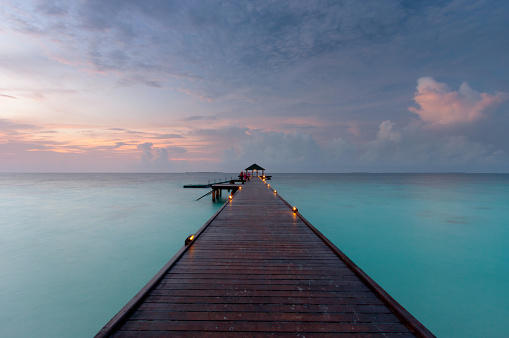 Evening descends upon a tropical island in the Maldives, and here we see a pier stretching out over the turquoise waters of the Indian Ocean.