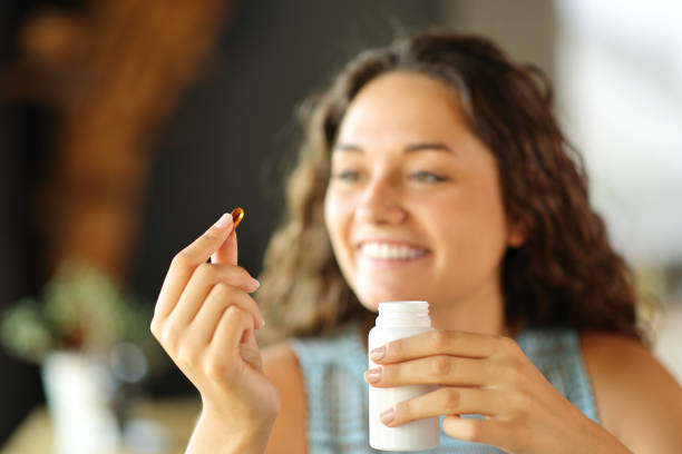 femme heureuse prête à manger une pilule de vitamines - vitamin pill nutritional supplement capsule antioxidant photos et images de collection