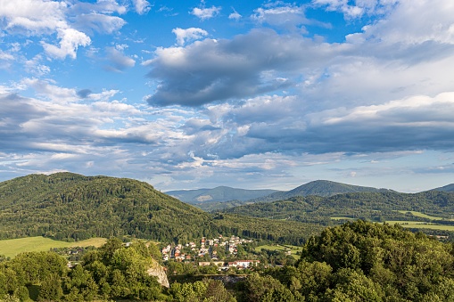 A drone shot of a little town surrounded with mountains covered in trees under a cloudy sky