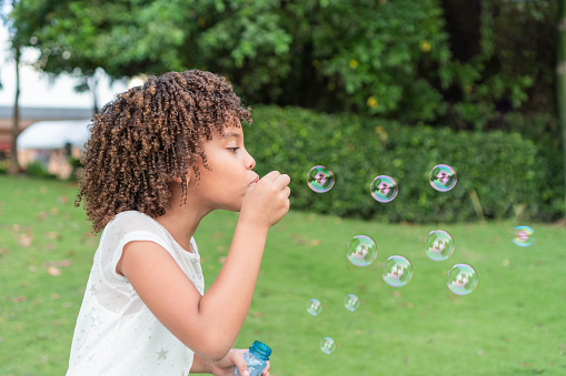 Little African American girl blowing bubbles in field