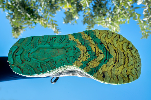 Close-up of the bottom tread of a woman's running shoe in mid stride against a blue sky during a run outdoors
